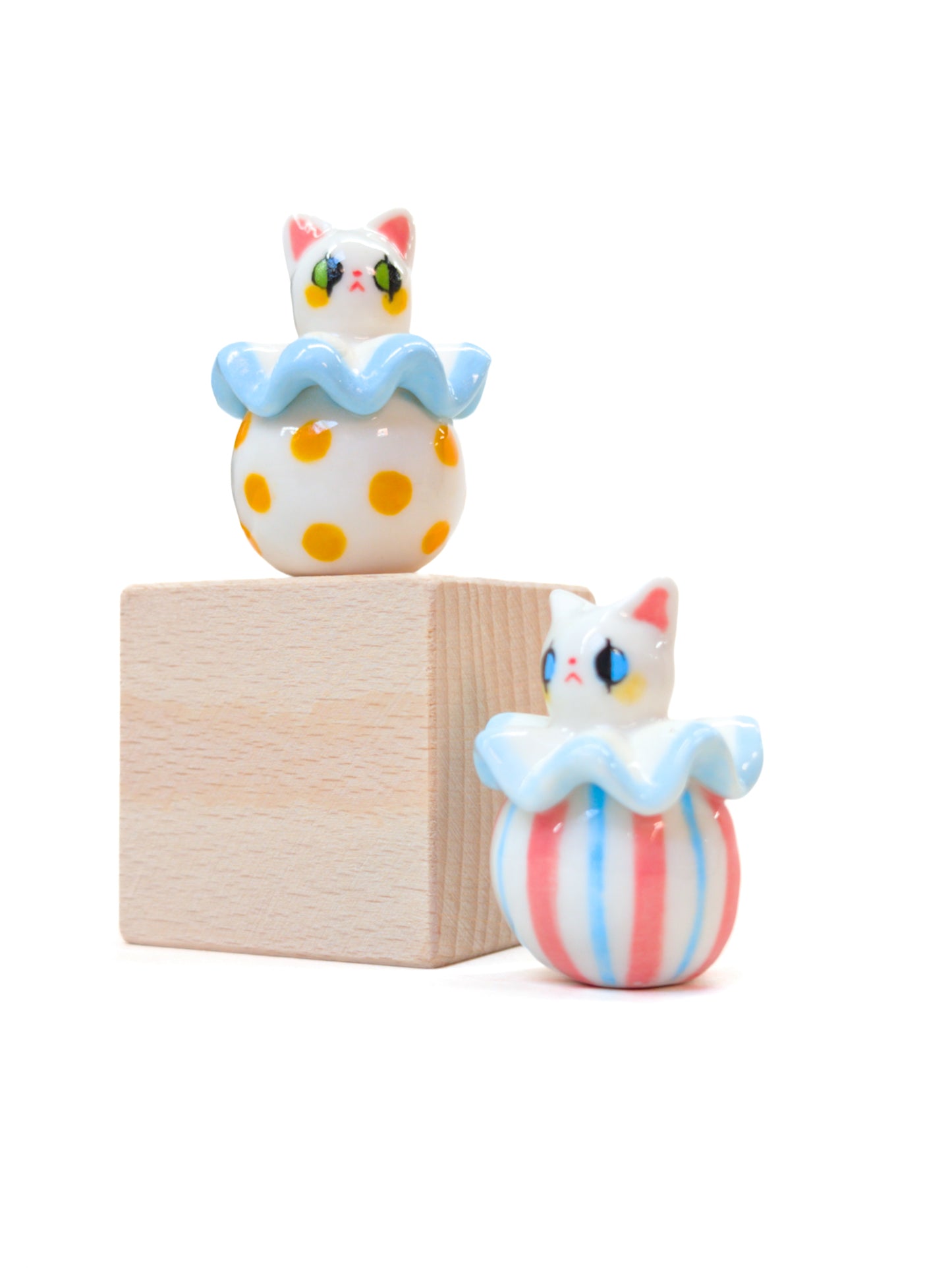 Two cat-shaped figurines on a wooden block with a white background